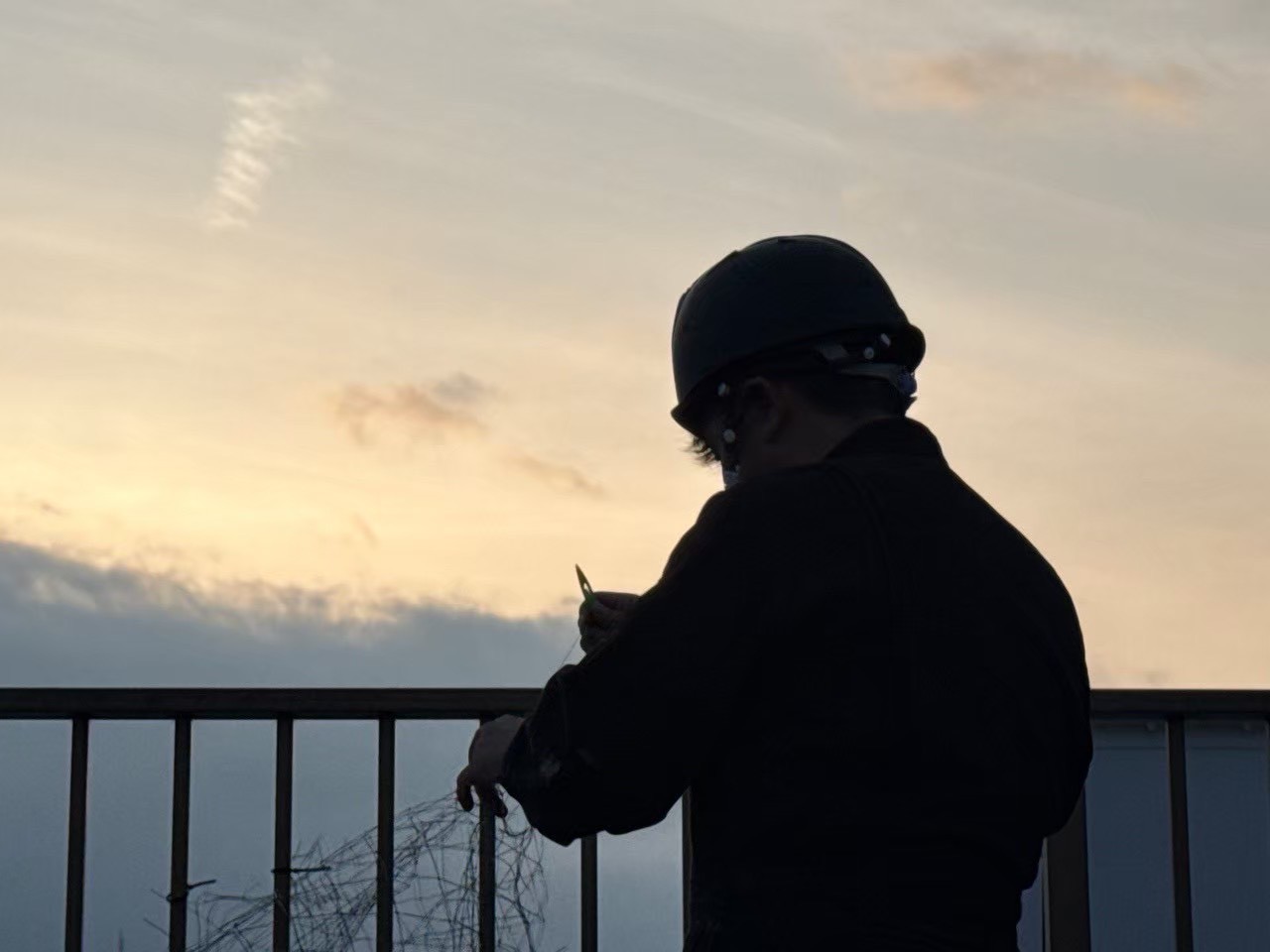 夕暮れ時の屋上でのネット結束作業：1日の施工完了に向けて最終調整を行う