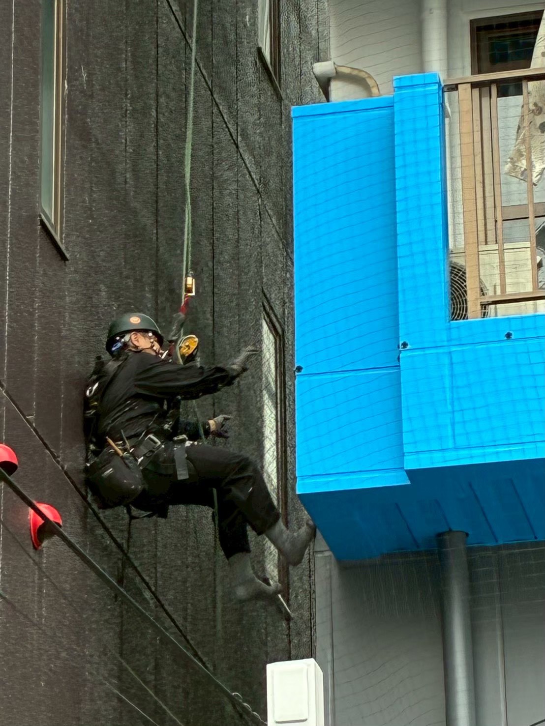 外壁隣接部での細部施工：ロープで宙吊りになりながら外壁の細部に金具を設置