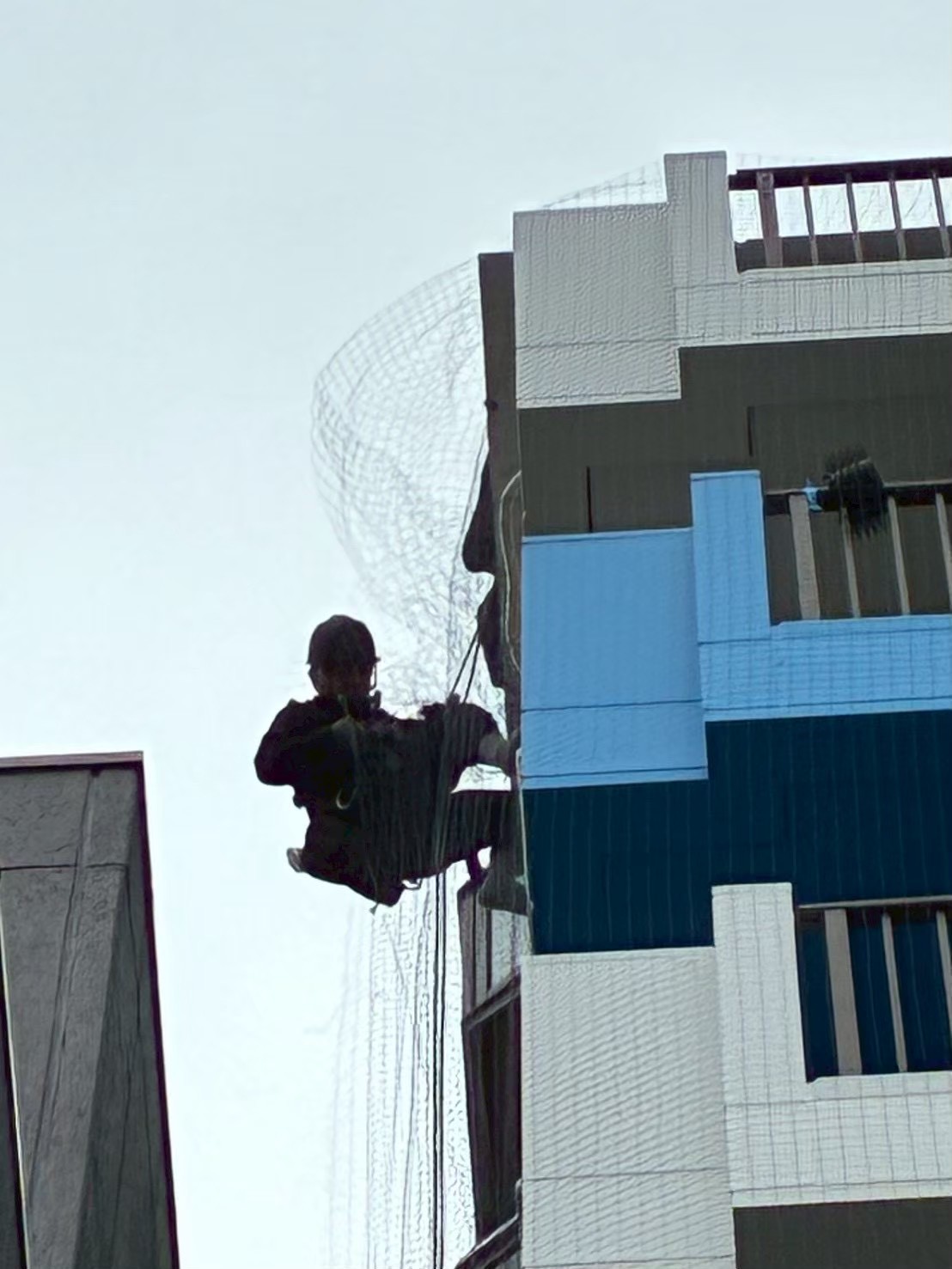 ネットの展開・位置決め作業：ロープで宙吊りになりながら大型ネットを外壁面に沿って展開