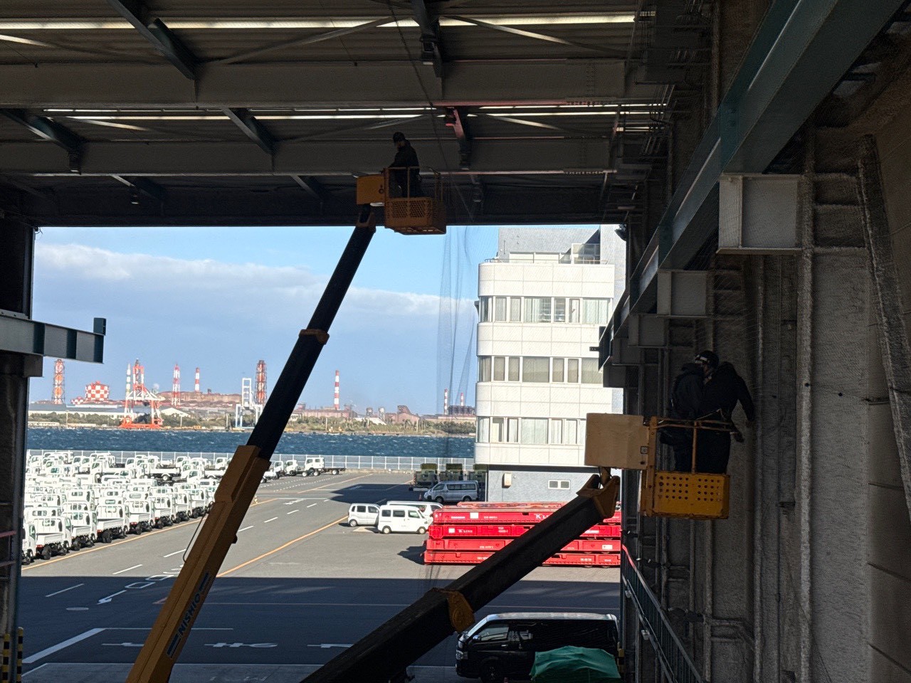 工場内複数台高所作業車による並行施工：奥行きのある工場内を複数チームで担当分けして施工