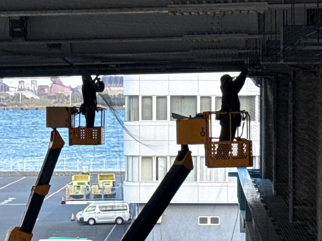 工場内大開口部・壁面上部への施工：複数台の高所作業車が連携して天井から壁面にかけてネットを張設