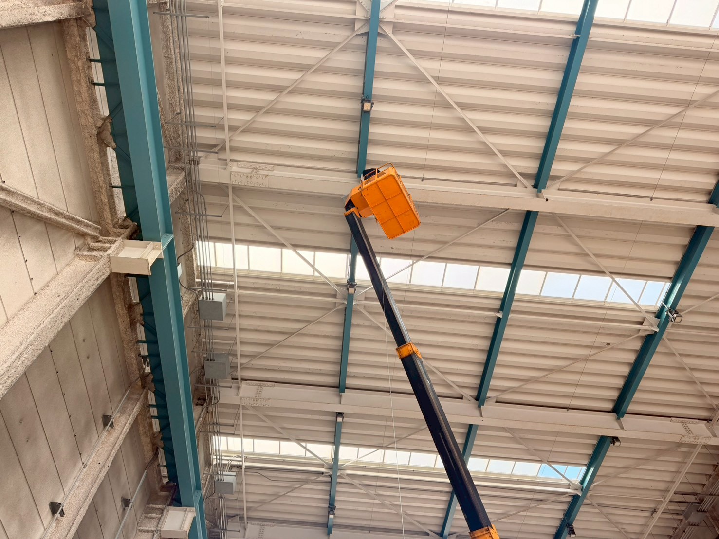 工場内天井面施工の全景：高所作業車のブームが伸びた状態で天井付近の施工を実施