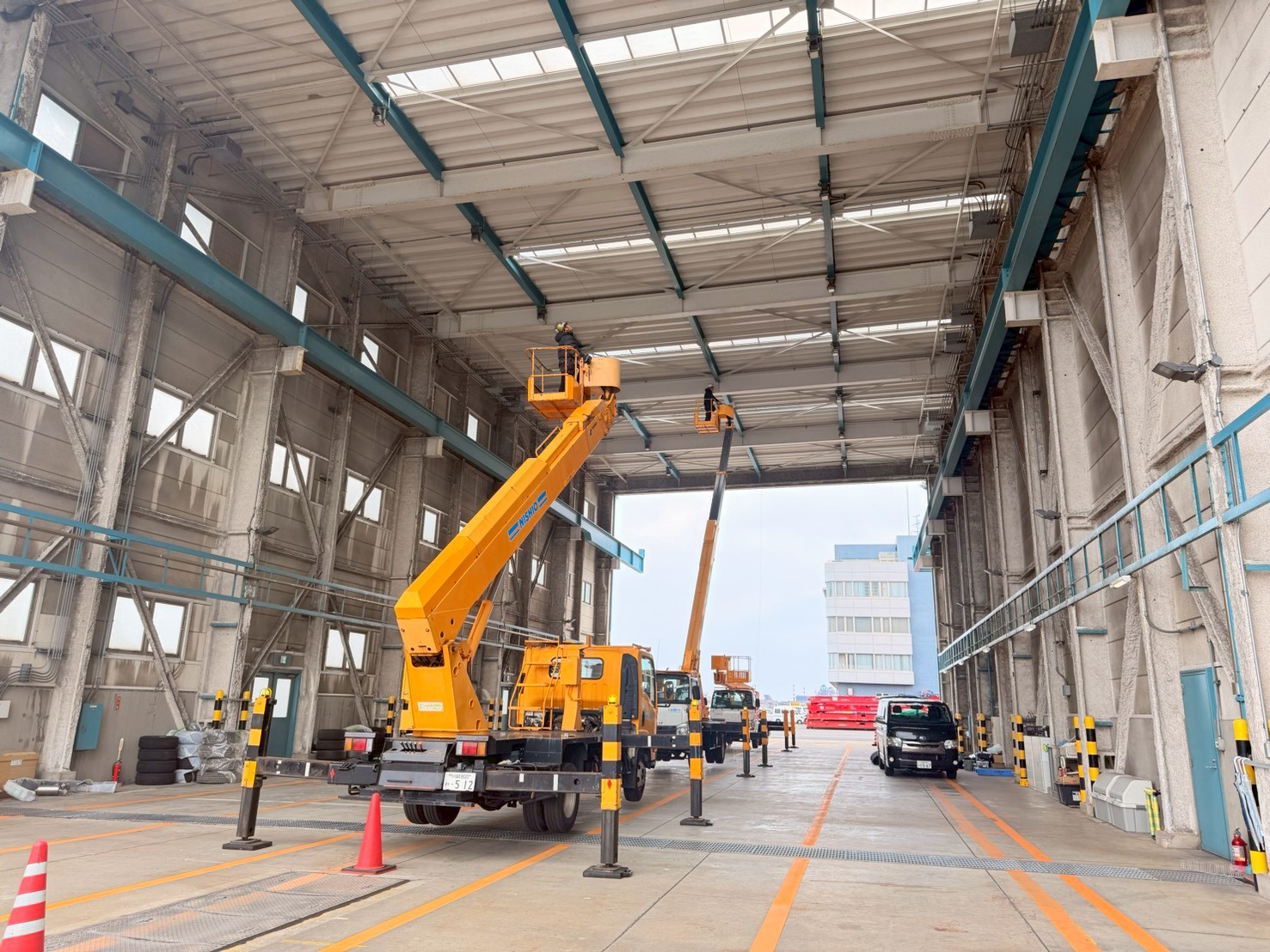 開口部上部フレームへの2台同時施工：左右から高所作業車が連携してネットを固定